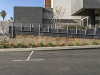 a person riding a skateboard near a wall and curb with landscaping in front of a building