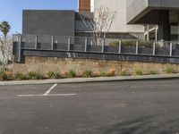 a person riding a skateboard near a wall and curb with landscaping in front of a building