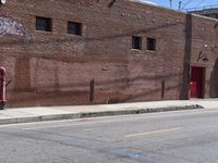 a red fire hydrant on the sidewalk of a brick building in the background is an old building with large windows