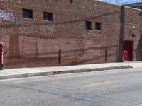 a red fire hydrant on the sidewalk of a brick building in the background is an old building with large windows