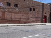 a red fire hydrant on the sidewalk of a brick building in the background is an old building with large windows