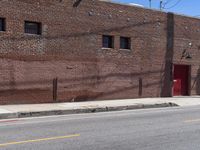 a red fire hydrant on the sidewalk of a brick building in the background is an old building with large windows