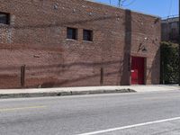 a red fire hydrant on the sidewalk of a brick building in the background is an old building with large windows