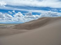 a lone horse is walking across sand dunes on a cloudy day under a partly blue sky