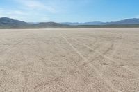 a motorcycle with dirt tires sits in the middle of a dry landscape with mountains in the background