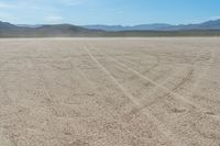 a motorcycle with dirt tires sits in the middle of a dry landscape with mountains in the background