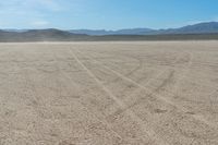 a motorcycle with dirt tires sits in the middle of a dry landscape with mountains in the background