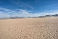 an empty desert with a dirt lot with mountains in the distance with white clouds above