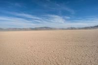 an empty desert with a dirt lot with mountains in the distance with white clouds above