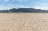 a large plain with dirt and mountains in the background and a few clouds in the sky