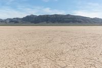 a large plain with dirt and mountains in the background and a few clouds in the sky