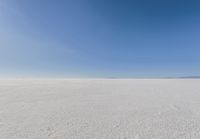 an empty sandy plain under a clear blue sky with a person on it using an umbrella