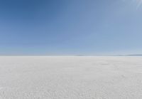 an empty sandy plain under a clear blue sky with a person on it using an umbrella