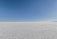 an empty sandy plain under a clear blue sky with a person on it using an umbrella