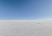 an empty sandy plain under a clear blue sky with a person on it using an umbrella