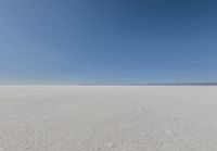 an empty sandy plain under a clear blue sky with a person on it using an umbrella