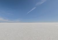 an empty sandy plain under a clear blue sky with a person on it using an umbrella