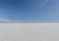 an empty sandy plain under a clear blue sky with a person on it using an umbrella