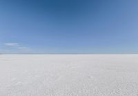 an empty sandy plain under a clear blue sky with a person on it using an umbrella