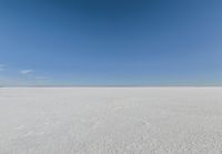 an empty sandy plain under a clear blue sky with a person on it using an umbrella