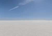 an empty sandy plain under a clear blue sky with a person on it using an umbrella