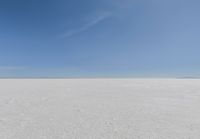 an empty sandy plain under a clear blue sky with a person on it using an umbrella