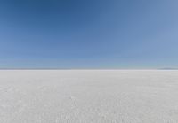 an empty sandy plain under a clear blue sky with a person on it using an umbrella