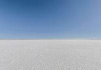 an empty sandy plain under a clear blue sky with a person on it using an umbrella