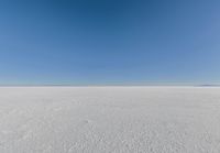 an empty sandy plain under a clear blue sky with a person on it using an umbrella