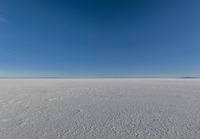 an empty sandy plain under a clear blue sky with a person on it using an umbrella