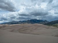 a person riding a horse in the middle of an area of sand dunes under a cloudy sky