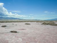 barren terrain is in the middle of an arid area with mountains in the background and clouds above