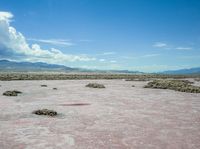 barren terrain is in the middle of an arid area with mountains in the background and clouds above