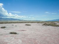 barren terrain is in the middle of an arid area with mountains in the background and clouds above