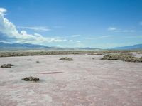 barren terrain is in the middle of an arid area with mountains in the background and clouds above