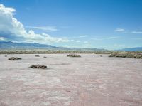 barren terrain is in the middle of an arid area with mountains in the background and clouds above