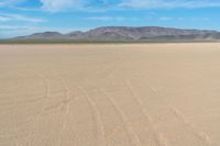 the sand looks like an unpaved beach under a blue sky with mountains in the background