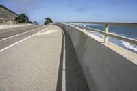 a curved sidewalk alongside the ocean with some cliffs in the distance and a bench in front