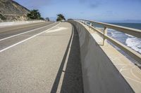 a curved sidewalk alongside the ocean with some cliffs in the distance and a bench in front