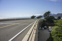 view of ocean from bridge of beach side street and road side area, with car parked next to it