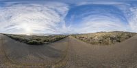 a panoramic image of a road in a desert land surrounded by bushes and a mountain