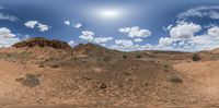 a mountain in the middle of a desert area and sky with clouds above it and below