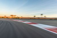 a photo of a dirt race track with sun setting in the distance of the track