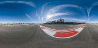 the 360 - view photo shows an asphalt track with clouds in the sky above it