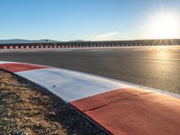 a photo of a dirt race track with sun setting in the distance of the track