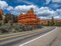 a road with some red rock formations in the background and blue skies above it and clouds above