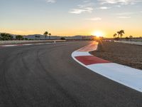 a photo of a dirt race track with sun setting in the distance of the track