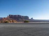 there is a lone motorcycle driving through the desert on a paved road near cliffs and buildings