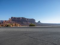 there is a lone motorcycle driving through the desert on a paved road near cliffs and buildings