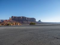 there is a lone motorcycle driving through the desert on a paved road near cliffs and buildings